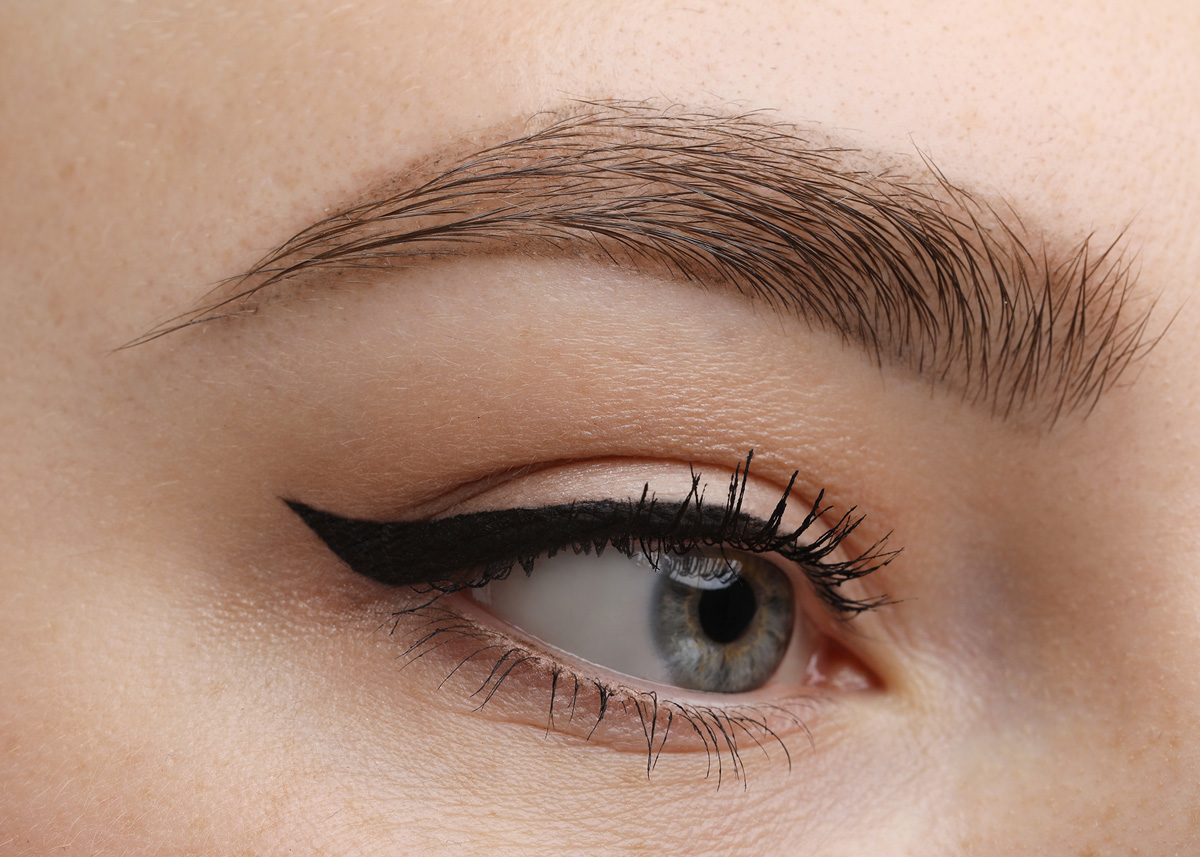 Close-up of precise black winged eyeliner on blue eye with long lashes and groomed brow